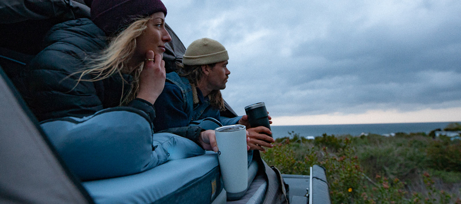 girl looking out of her roof top tent with a coffee cup